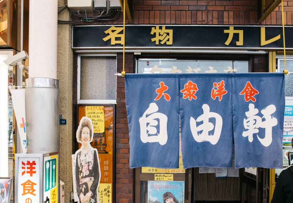Narrow entrance of Jiyuken curry restaurant with a blue noren curtain in Namba