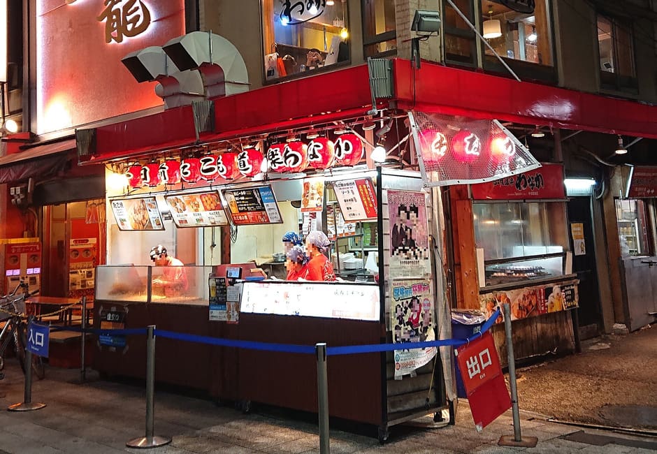 Takoyaki Wanaka Sennichimae main shop front with red awning and signs at night, Namba, Osaka