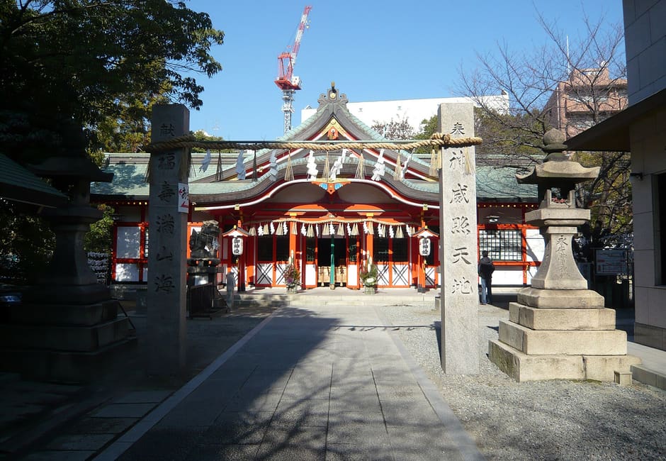 Red haiden hall of Tamatsukuri Inari Shrine seen across the stone-paved precinct on a sunny day