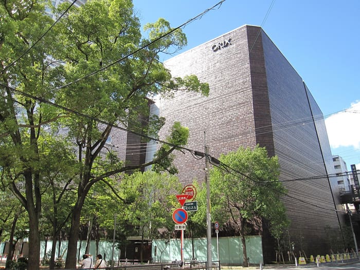 Brown brick ORIX Theater building with its lettering seen through street trees in daylight