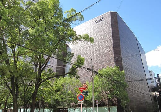 Brown brick ORIX Theater building with its lettering seen through street trees in daylight